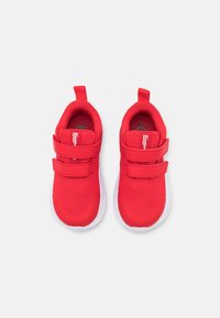 Zapatillas deportivas rojas con parte superior de tela de malla, doble correa de Velcro y pestaña para tirar; suela de goma blanca con patrón de relieve.