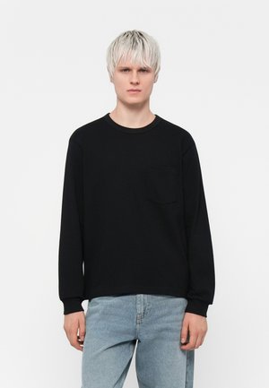 Black long-sleeve shirt with a round neck and a chest pocket, made of smooth fabric. Paired with light blue denim jeans.