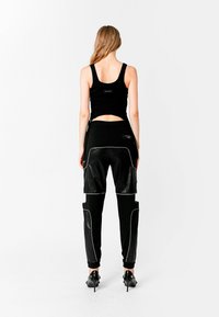 Top corto negro sin mangas con un corte, combinado con pantalones negros de acabado de cuero brillante y costuras blancas.