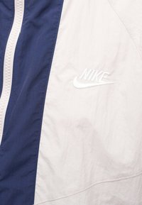 Nike jakna s tamnoplavim i svijetloružičastim blok dizajnom. Ima teksturirani, lagani materijal i izvezenu oznaku na prsima.