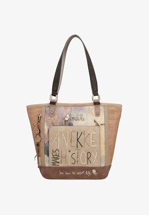 Sac cabas beige et marron avec lettrage artistique "Anekke fait l'histoire" et détails de breloques suspendus à une sangle latérale.