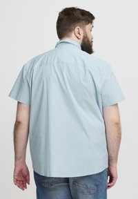 Cămașă bleu deschis, cu mâneci scurte, din bumbac, cu guler cu nasturi, design simplu, fără motive vizibile, croială lejeră, vedere din spate.
