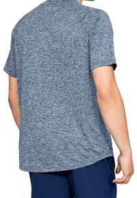 Hombre que lleva una camiseta deportiva de manga corta en gris jaspeado y pantalones cortos azul marino, de espaldas a la cámara.