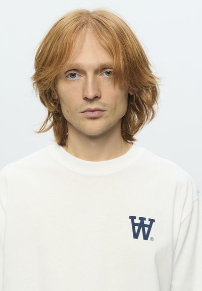 Felpa bianca con scollo rotondo e un logo blu navy sul petto. Il tessuto appare morbido, con una superficie leggermente strutturata.