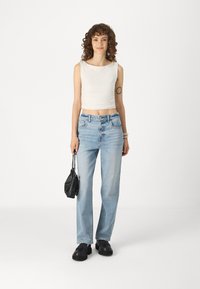 Jeans din denim de culoare albastru deschis, cu o croială relaxată, asortați cu un top alb fără mâneci. Modelul ține o geantă mică de mână neagră și poartă pantofi negri.