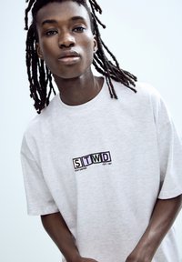 Gray short-sleeve t-shirt with a printed logo reading "STWD" in colorful square designs. Soft texture with a relaxed fit.