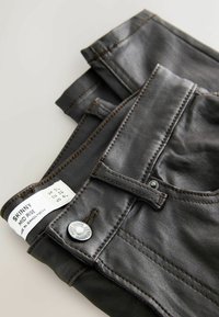 Blugi skinny negri cu talie medie, detaliu cu buton argintiu și cusături maro. Eticheta de îngrijire este vizibilă pe talie. Textură netedă.