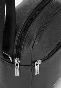 Borsa sintetica nera con texture, dotata di più cerniere, hardware argento e un design elegante. Presenta un marchio ben visibile sui tiranti delle cerniere.