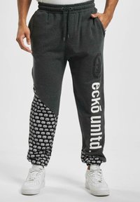 Grå sweatpants med en tapered fit, der har et sort mønstrede sidepanel, hvid tekst, elastisk talje og snøre.