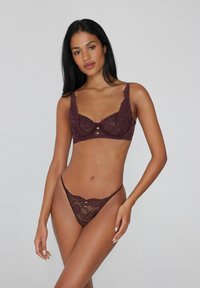 Burgundské krajkové podprsenky s kosticemi a širokými ramínky, se zdobeným okrajem a dekorativními knoflíčky uprostřed. Ladící tanga s krajkovým lemem.