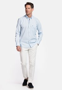 Lichtblauwe button-up overhemd met een zak, gecombineerd met witte broek en zwarte instap schoenen. Casual ontwerp met een zachte textuur.