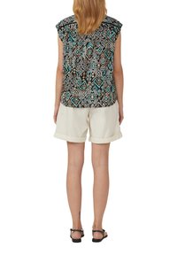 Camicetta nera e turchese a fantasia con maniche arricciate, abbinata a pantaloni corti beige arrotolati. Modella che indossa sandali neri, vista da dietro.