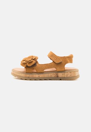Sandal din suede maro cu detaliu floral, curea ajustabilă, platformă cu textură de plută și talpă din cauciuc. Design deschis pentru respirabilitate.