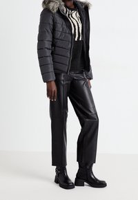 Donsjack in donkergrijs met een met bont gevoerde capuchon, gecombineerd met een zwarte trui met een zebrapatroon, en zwarte leren broek en laarzen.