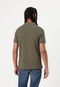 Olivgrön polotröja med krage, korta ärmar och rak fåll. Buren med blå jeans, visad från baksidan och flätat hår.