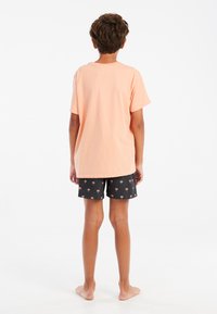 Lichtoranje katoenen t-shirt en zwarte shorts met palmbomenpatroon. Het t-shirt heeft korte mouwen en een losse pasvorm.