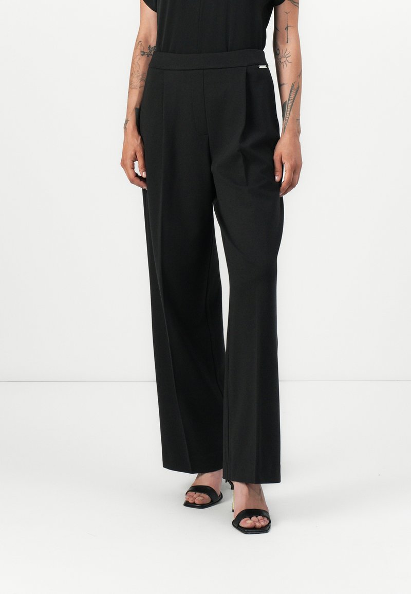 Black wide-leg trousers made of smooth fabric, featuring a flat front, side pockets, and a subtle silver accent on the waistband.