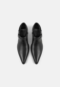 Stivali alla caviglia in pelle nera con punta appuntita, finitura liscia, dettaglio di fibbia regolabile sul lato, suola piatta. Logo del marchio visibile all'interno.