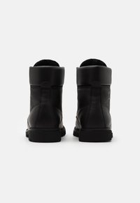 Botas de tobillo de cuero negro con un collar acolchado, superficie texturizada, suela de goma y un diseño minimalista que presenta un logotipo discreto en el costado.