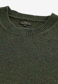 Pull en laine d'agneau côtelé vert foncé avec col rond et étiquette noire indiquant « Next Signature », taille moyenne.