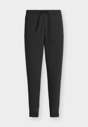 Black tapered sweatpants with elastic waistband, drawstring, side pockets, and ribbed cuffs isolated on a light background.
