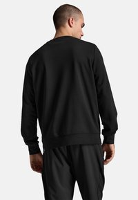 Sort sweatshirt med lange ærmer, rund hals og ribbede manchetter. Glat stof, afslappet pasform og en ensfarvet rygdesign. Sammen med sorte bukser.