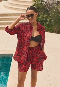 Rode en zwarte luipaardprint shorts en een bijpassend oversized shirt, gemaakt van lichtgewicht stof, met zakken en een cropped ontwerp.