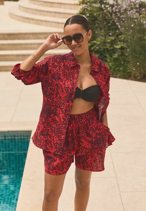 Rode en zwarte luipaardprint shorts en een bijpassend oversized shirt, gemaakt van lichtgewicht stof, met zakken en een cropped ontwerp.
