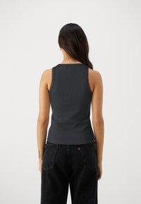 Mørk grå ribbestrikket tanktopp med rund hals og brede stropper, sammen med høyt liv svarte jeans. Enkel og figursydd design.