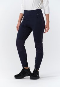 Námořnické sportovní kalhoty s vysokým pasem, elastickým pasem, kapsou na zip a kontrastním tmavším panelem na koleni. V kombinaci s černými sportovními botami.
