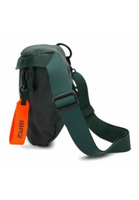 Bolso cruzado de tela verde con correa ajustable, cremallera lateral y una etiqueta naranja. Presenta un diseño redondeado y una textura duradera.