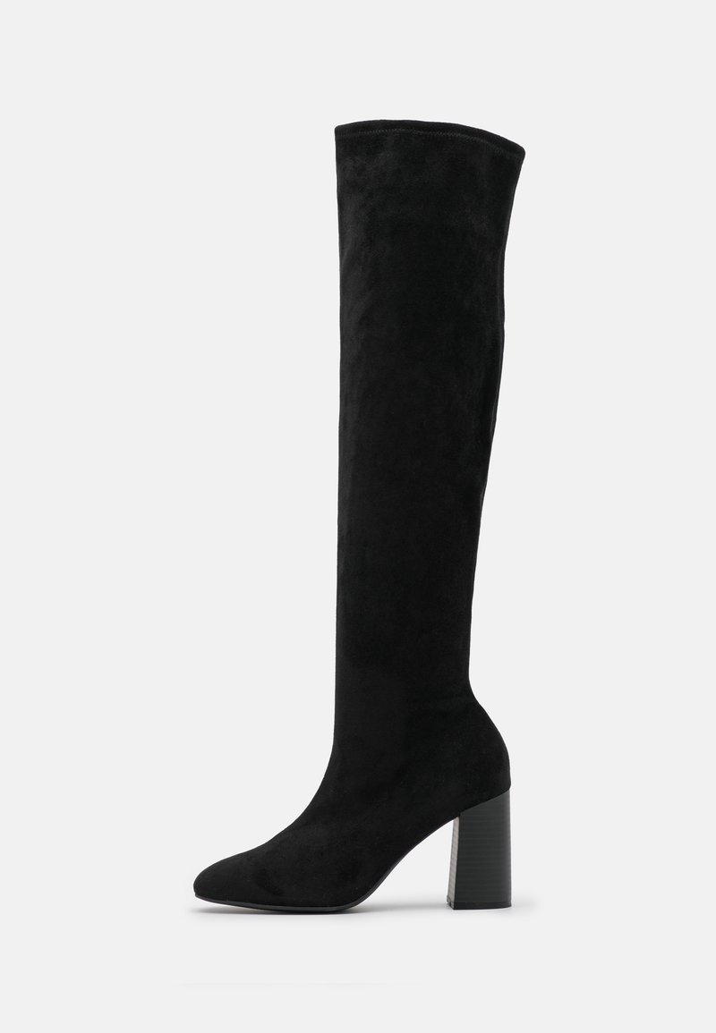 Botte noire en daim montant jusqu'au genou avec talon bloc et bout pointu, vue de profil sur un fond uni.
