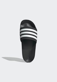 Svart slidesandal med en texturerad yta, med tre vita ränder tvärs över toppen. Varumärkeslogotypen är präglad på sulan.