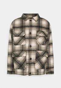 Rutig skjortjacka i beige, svart och krämfärgad. Har en krage, fem knappar och två framfickor. Mjuk, texturerad tyg.