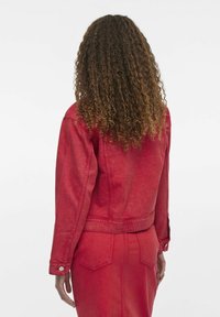 Rød denimjakke med cropped design og lange ærmer, med en enkelt knap ved manchet og synlige syningsdetaljer.