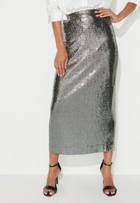 Zilveren pailletten midi rok met een aansluitende taille en rechte silhouet, gedragen met een witte blouse en zwarte sleehakken.