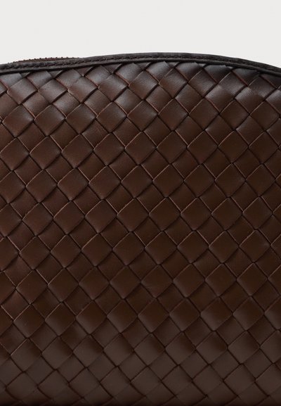 Σκούρα καφέ δερμάτινη επιφάνεια με πυκνό πλεκτό μοτίβο καλαθιού και στρογγυλεμένη λεπτομέρεια ραμμένης άκρης.