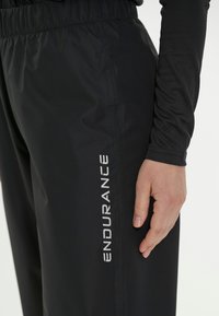 Svarta träningsbyxor med texturerad tyg, elastisk midja och en vit "ENDURANCE"-logo på sidan. Har en slim fit-design.