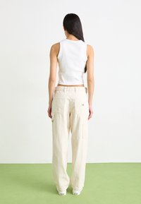 White ribbed tank top paired with cream-colored, striped, wide-leg cargo pants. Pants feature back pockets and a small logo detail.