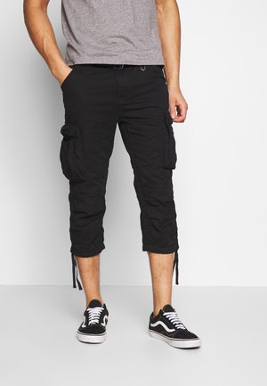 Pantaloni cargo neri con vestibilità rilassata, numerose tasche laterali, lunghezza cropped e polsini regolabili con coulisse. Abbinati a sneakers nere.