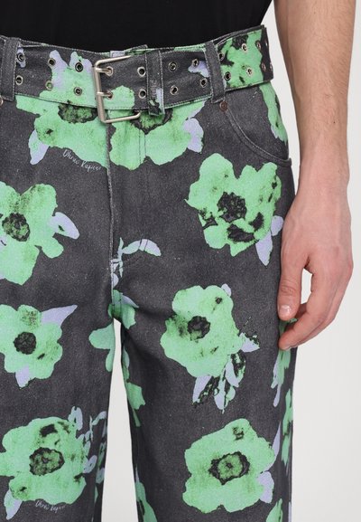 Hose mit floralen Druck zeigt eine schwarze Grundfarbe mit großen grünen Blumen, ergänzt durch einen silbernen Schnallen-Gürtel mit Ösen und geradem Schnitt.