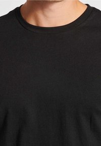 Černé bavlněné tričko s kulatým výstřihem. Má hladkou texturu a standardní krátké rukávy. Jednoduché, jednobarevné bez vzorů.