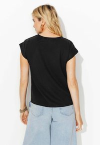 Haut noir à manches courtes en tissu lisse. Doté d'un col rond et d'une coupe décontractée, associé à un jean large bleu clair.