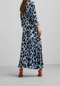 Abito maxi in tessuto blu chiaro con motivo leopardato in nero, blu e ruggine. Presenta maniche lunghe e una silhouette fluida.