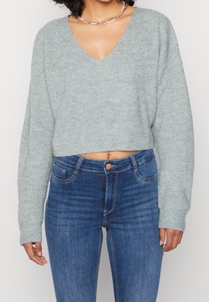 Lichtgrijze cropped trui met een geribbeld patroon en V-hals ontwerp, gecombineerd met donkerblauwe high-waisted jeans.
