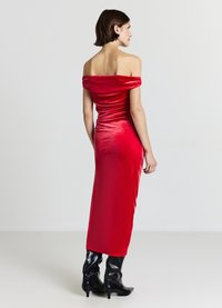 Rotes schulterfreies Kleid aus glattem Stoff, figurbetont, knielang, mit einem dezenten Glanz und getragen mit kniehohen schwarzen Stiefeln.