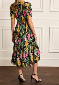 Abito midi floreale con corpino aderente, maniche a sbuffo e gonna a strati. Presenta colori vivaci tra cui verde, rosa, giallo e nero.