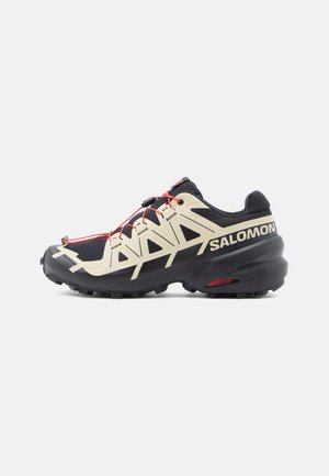 Czarne i kremowe buty sportowe z teksturowaną cholewką, czerwonymi sznurówkami oraz wyraźną podeszwą z przyczepnością. Charakteryzują się eleganckim designem z wzmocnionym noskiem.