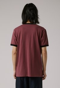 Maroon T-shirt with a black ribbed collar and sleeve hems. Short sleeves and a relaxed fit, made from soft cotton fabric.