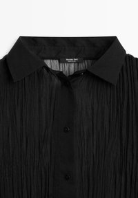 Schwarzes, gekräuseltes Hemd mit klassischem Kragen, ausgestattet mit fünf schwarzen Knöpfen und dezenten Falten, aus einem leichten, strukturierten Stoff gefertigt.
